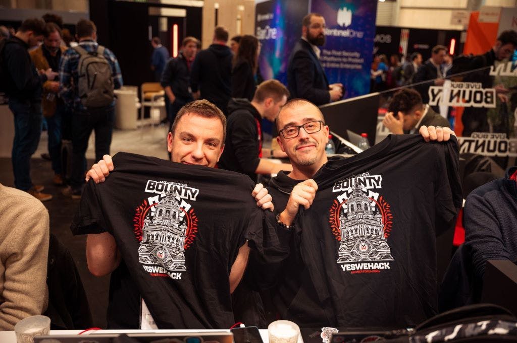 Two ethical hackers hold up t-shirts at the YesWeHack Live Bug Bounty for Groupe Caisse des Dépôts at InCyber Forum (FIC) Europe, in Lille, in 2024